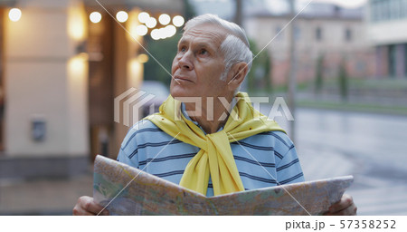 Senior male tourist exploring town with a map in hands and looking for the route 57358252