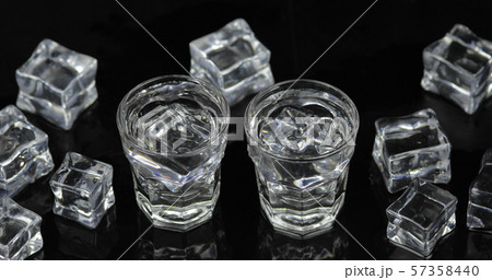 Shots of vodka with ice cubes against black background Shots of vodka with ice cubes against black background 57358440