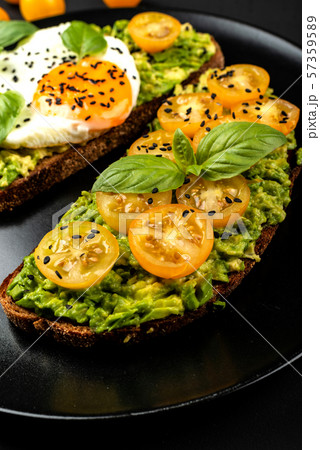Open sandwiches with avocado guacamole, yellow cherry tomatoes, fried egg and basil on a black plate Open sandwiches with avocado guacamole, yellow cherry tomatoes, fried egg and basil on a black plate 57359589