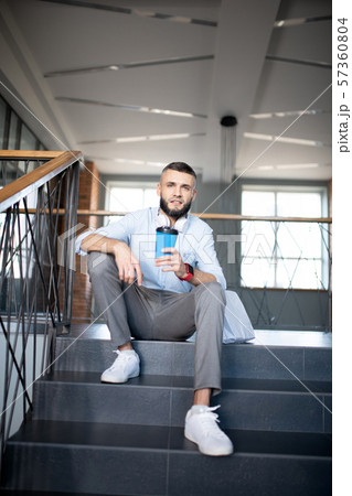 Office worker sitting on stairs and drinking takeaway coffee Office worker sitting on stairs and drinking takeaway coffee 57360804