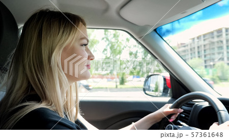 Blonde young woman is driving a car in the city holding hands on steering wheel. Blonde young woman is driving a car in the city holding hands on steering wheel. 57361648