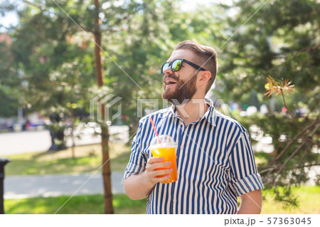 Portrait of a positive cheerful young man with a glass of juice with a straw while walking in the 57363045
