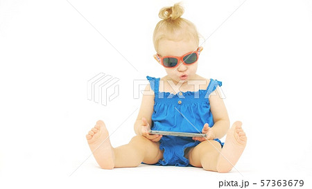 Serious baby wearing sunglasses looks at the smartphone 57363679