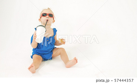Cool baby girl wearing sunglasses drinks from paper cup with a straw against white background 57444357