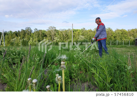 The headphone and glasses worker mows the grass in 57456810