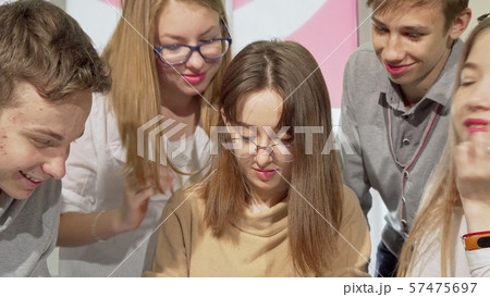 Teenage girl writing in her textbook with her classmates surrounding her 57475697