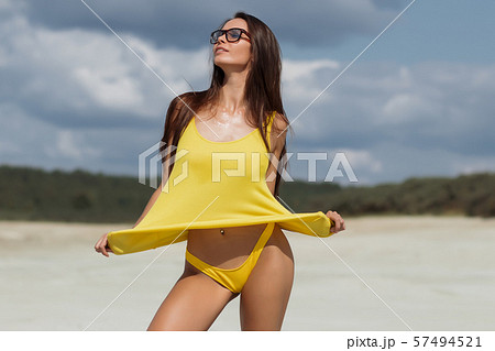 Hot woman in stylish swimsuit raising top on beach Hot woman in stylish swimsuit raising top on beach 57494521