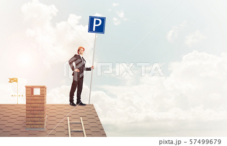 Young businessman with parking sign standing on brick roof. Mixe 57499679