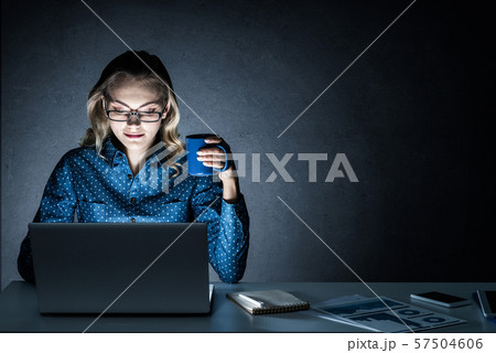 Attractive blonde working on laptop in dark office. Mixed media Attractive blonde working on laptop in dark office. Mixed media 57504606