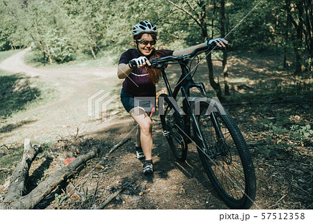 Photo of sportswoman in helmet raising bicycle to hill in forest Photo of sportswoman in helmet raising bicycle to hill in forest 57512358