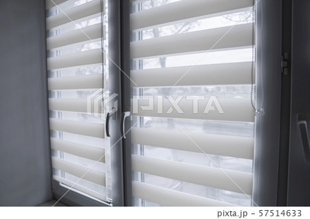 White fabric roller blinds on the white plastic window in the living room. Roll curtains indoor. 57514633