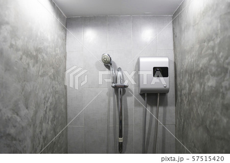 Instant tankless electric water heater installed on grey tile wall with input and output pipe/outlet 57515420