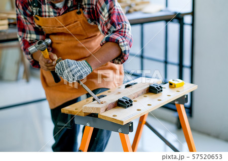 Old craftsman use hammer and chisel to work with wood and produce some product in his workplace 57520653
