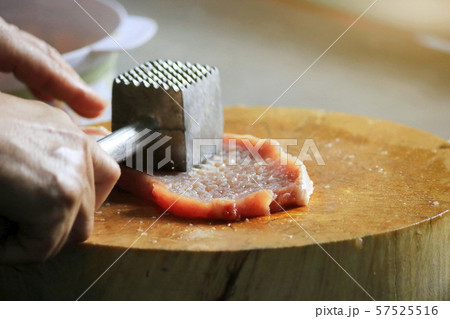 The man's hand picks up an iron hammer and smashed the pork on a wooden chopping board to make steak. The man's hand picks up an iron hammer and smashed the pork on a wooden chopping board to make steak. 57525516