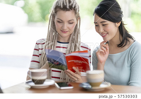 オープンテラスのカフェでコーヒーブレイクを楽しむ外国人女性と笑顔で会話する日本人女性 57530303