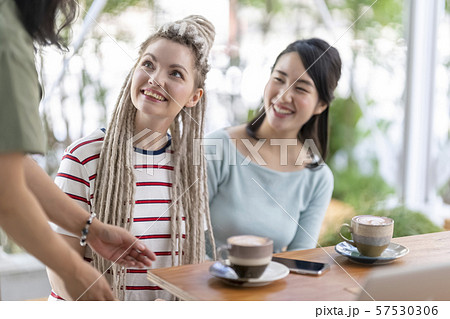 カフェの店員からおもてなしを受けて笑顔になる外国人と日本の友達の写真素材