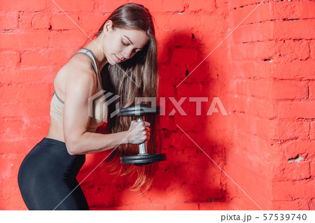 A sports girl holds dumbbells in his arms, shaking muscle. On a scarlet background. Has long black 57539740