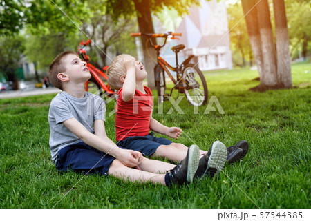 Two boys look up sitting on the grass. Bicycles in 57544385