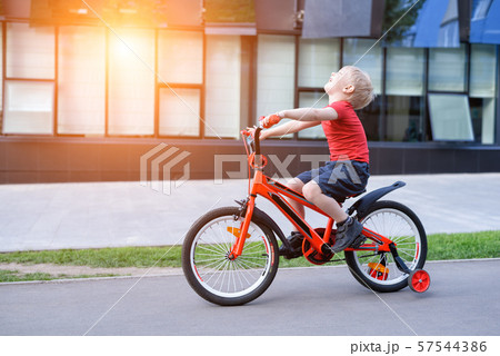 Handsome blond boy rides on a children's bicycle. 57544386
