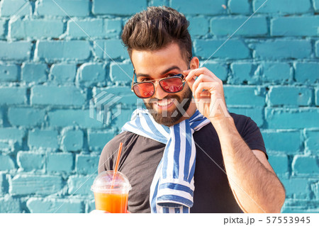 Cute stylish arab young male hipster with a mustache and a beard and wearing glasses drinking juice 57553945