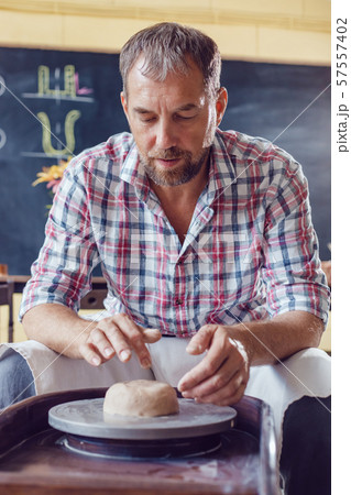A male potter works on a pottery wheel in a workshop. 57557402