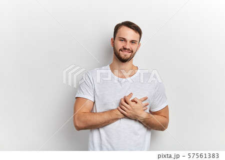 attractive cheerful young man has friendly expression, keeps palms on heart 57561383