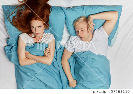 depressed girl with crossed arms lying on the bed with her sleeping husband depressed girl with crossed arms lying on the bed with her sleeping husband 57563110