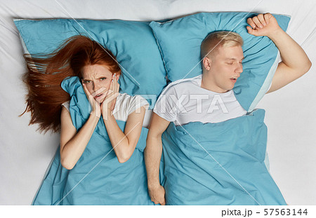 Unhappy woman closing her ears with palms and her snoring husband lying bedroom. Unhappy woman closing her ears with palms and her snoring husband lying bedroom. 57563144