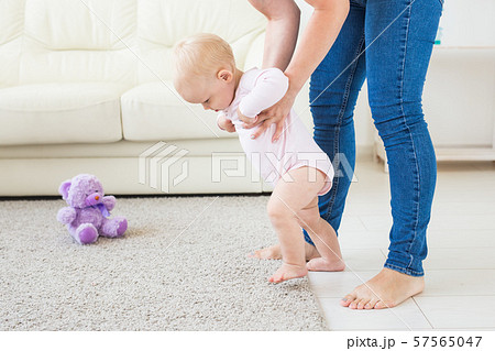 First steps of baby toddler learning to walk in white sunny living room. Footwear for child. 57565047