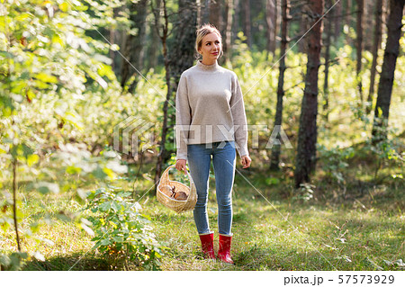 woman with basket picking mushrooms in forest 57573929