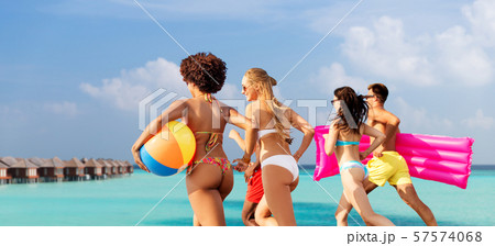 friends run with beach ball and swimming mattress 57574068