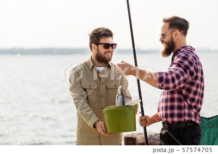 male friends with fish and fishing rods on pier 57574705
