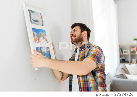 man hanging picture in frame to wall at home 57574726