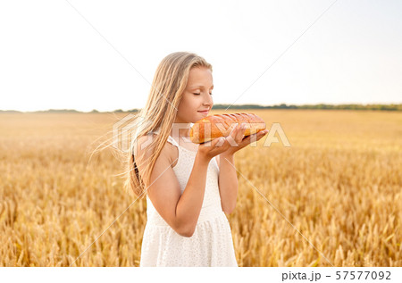 girl smelling loaf of white bread on cereal field 57577092