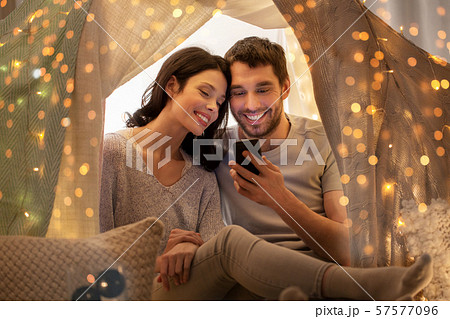happy couple with smartphone in kids tent at home 57577096