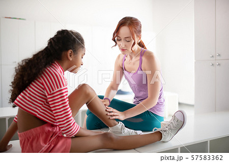 Red-haired PE teacher helping girl with knee trauma Red-haired PE teacher helping girl with knee trauma 57583362