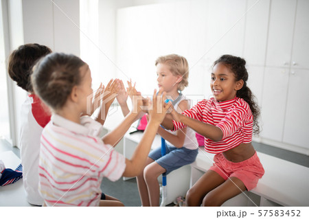 Boys and girls clapping their hands while sitting in locker room Boys and girls clapping their hands while sitting in locker room 57583452