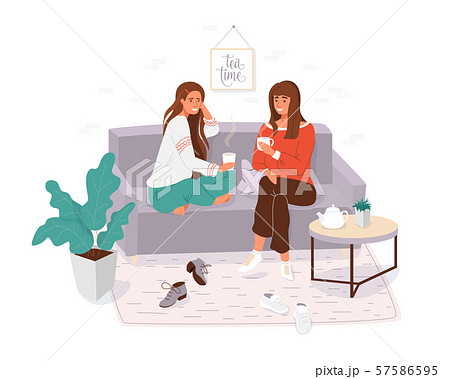 Two young women spending time together. Girls cosy sitting on the couch, talking and holding cup tea Two young women spending time together. Girls cosy sitting on the couch, talking and holding cup tea 57586595