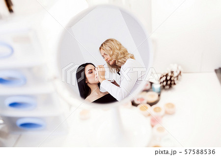 Make-up artist applying bright base color eyeshadow on model's eye and holding a shell with Make-up artist applying bright base color eyeshadow on model's eye and holding a shell with 57588536