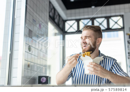 Positive young stylish guy eating chinese noodles in a cafe during a break at work. The concept of Positive young stylish guy eating chinese noodles in a cafe during a break at work. The concept of 57589814
