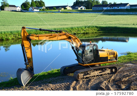 Excavator by the river against the green field Excavator by the river against the green field 57592780