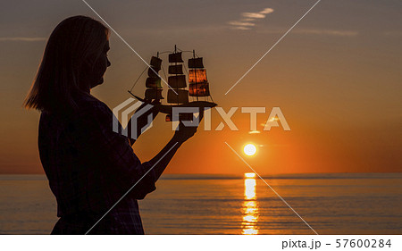 A woman stands by the sea at sunset, holds in her hands a model of a sailing ship. Hope and travel 57600284