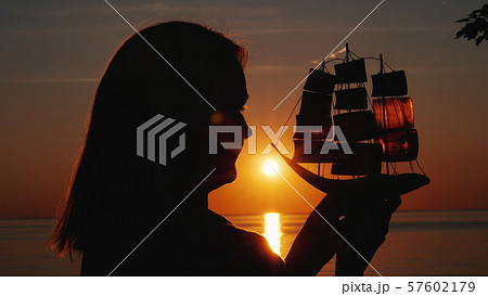 Profile of a woman with a toy sailboat against the setting sun Profile of a woman with a toy sailboat against the setting sun 57602179