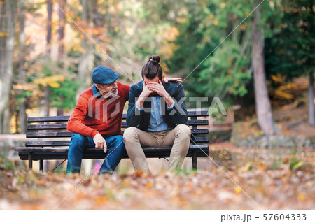 Senior father comforting his sad adult son on bench in nature. Senior father comforting his sad adult son on bench in nature. 57604333