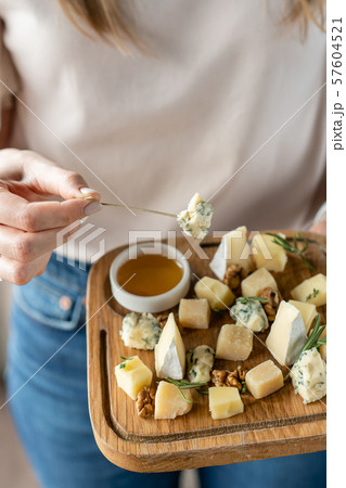 Girl holding piece of Gorgonzola cheese on a skewer and wooden plate with cheese. Delicious cheese Girl holding piece of Gorgonzola cheese on a skewer and wooden plate with cheese. Delicious cheese 57604521