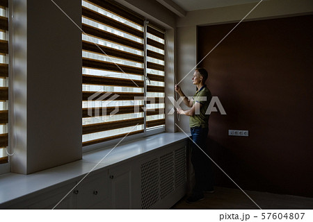 The man is opening  the blinds. 57604807