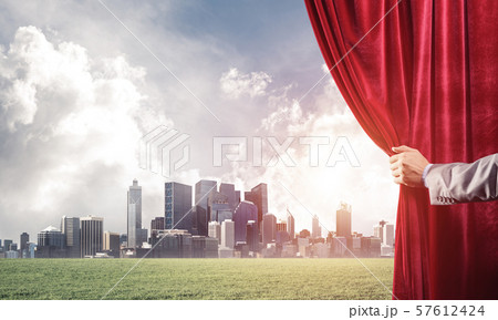 Green meadow behind red curtain and hand holding it Green meadow behind red curtain and hand holding it 57612424