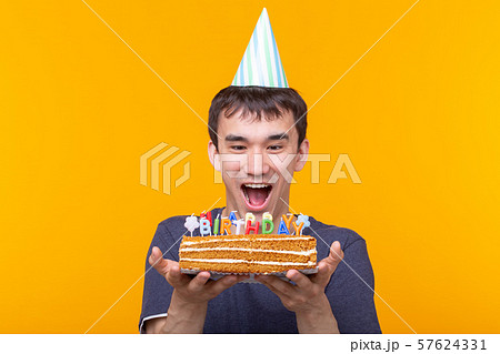 Portrait of a funny positive guy with a paper cap and glasses holding a congratulatory homemade cake 57624331