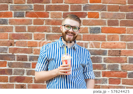Blurred positive young hipster man with beard and mustache in glasses holding a fruit milkshake in Blurred positive young hipster man with beard and mustache in glasses holding a fruit milkshake in 57624425
