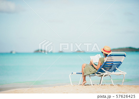 Young woman reading book on chaise-lounge on the beach Young woman reading book on chaise-lounge on the beach 57626425